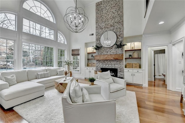 living room with a stone fireplace, a towering ceiling, built in features, a chandelier, and light hardwood / wood-style floors