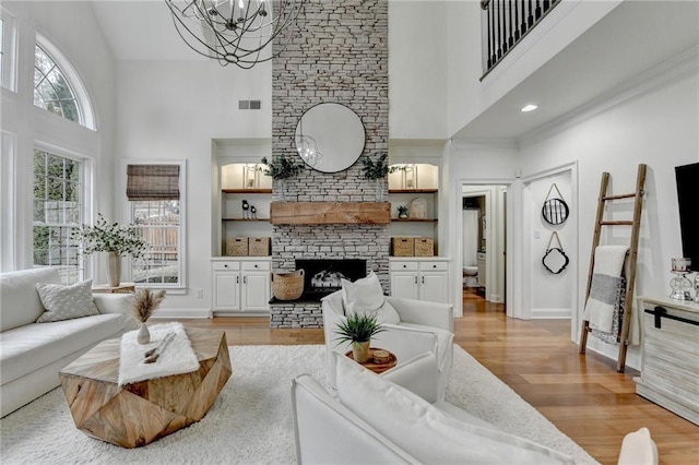 living room featuring built in shelves, light wood-type flooring, a notable chandelier, a fireplace, and a high ceiling