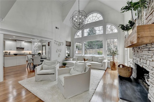 living room featuring a high ceiling, a fireplace, an inviting chandelier, and light hardwood / wood-style floors