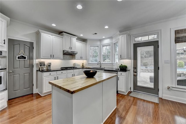 kitchen featuring butcher block countertops, white cabinetry, decorative backsplash, stainless steel appliances, and light hardwood / wood-style flooring