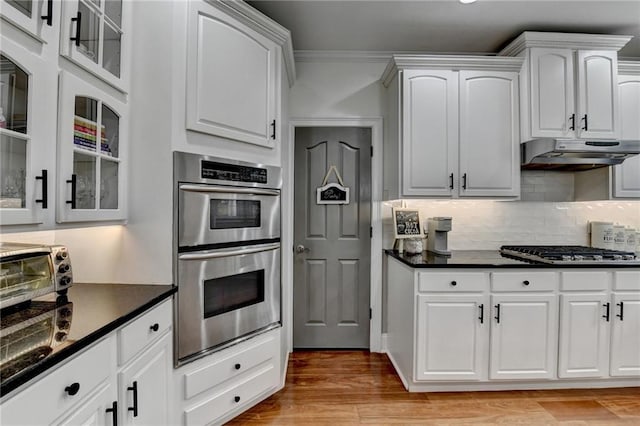 kitchen with white cabinetry, decorative backsplash, ornamental molding, light hardwood / wood-style floors, and stainless steel appliances