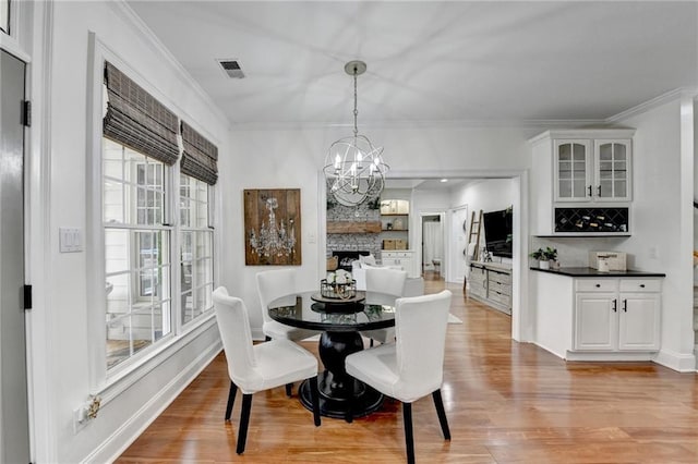 dining space featuring crown molding, a fireplace, a chandelier, and light wood-type flooring