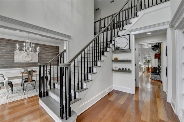 staircase featuring a towering ceiling, wood-type flooring, ornamental molding, and a chandelier