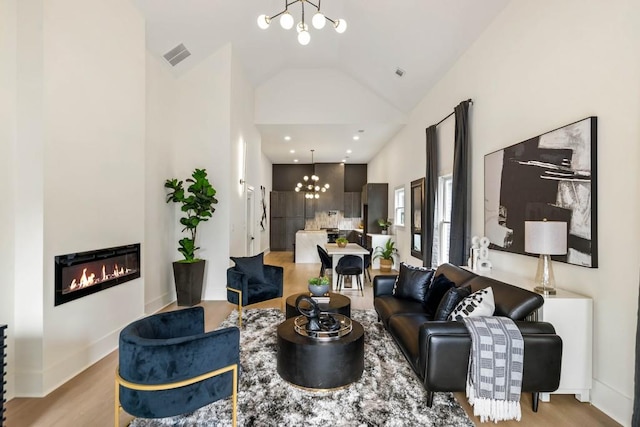 living room featuring a glass covered fireplace, an inviting chandelier, light wood-style floors, and visible vents