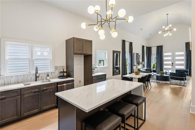 kitchen with light stone countertops, a sink, dark brown cabinets, dishwasher, and a chandelier