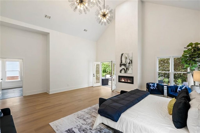 bedroom with wood finished floors, visible vents, high vaulted ceiling, a notable chandelier, and a large fireplace