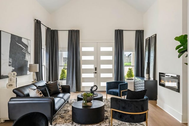 living room featuring a glass covered fireplace, wood finished floors, baseboards, and high vaulted ceiling