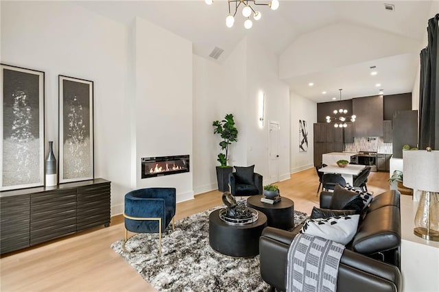 living room with visible vents, light wood-style floors, an inviting chandelier, and a glass covered fireplace