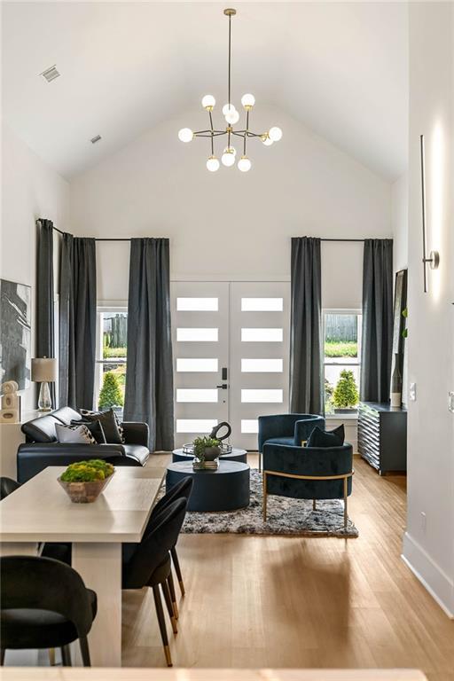 dining area featuring visible vents, baseboards, light wood-style floors, an inviting chandelier, and high vaulted ceiling