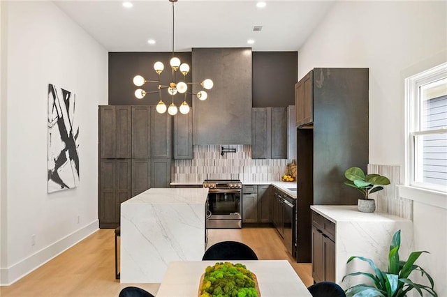 kitchen featuring light stone countertops, electric range, light wood-style flooring, a notable chandelier, and tasteful backsplash