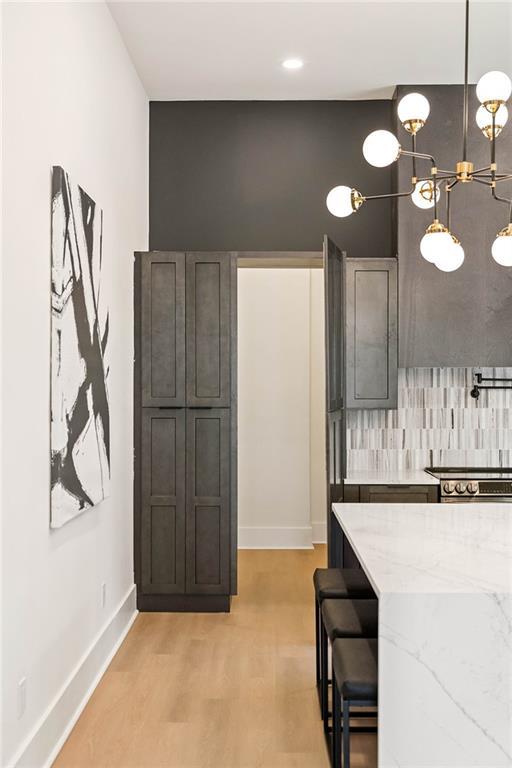 kitchen with baseboards, light stone countertops, a breakfast bar area, light wood-type flooring, and decorative backsplash