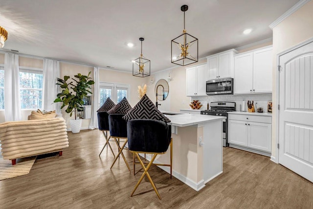 kitchen with a kitchen bar, white cabinetry, stainless steel appliances, hanging light fixtures, and ornamental molding