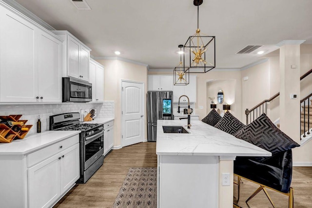 kitchen with white cabinets, appliances with stainless steel finishes, decorative light fixtures, tasteful backsplash, and an island with sink