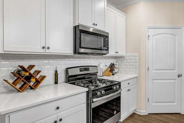 kitchen with dark hardwood / wood-style flooring, appliances with stainless steel finishes, backsplash, white cabinetry, and ornamental molding