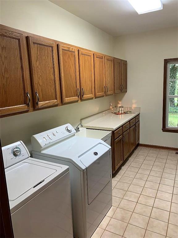 clothes washing area with light tile floors, washing machine and dryer, cabinets, and sink