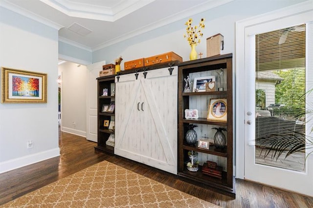 interior space with a barn door, baseboards, a tray ceiling, dark wood finished floors, and crown molding