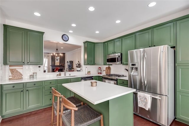 kitchen with dark wood-style flooring, stainless steel appliances, light countertops, a sink, and a kitchen island