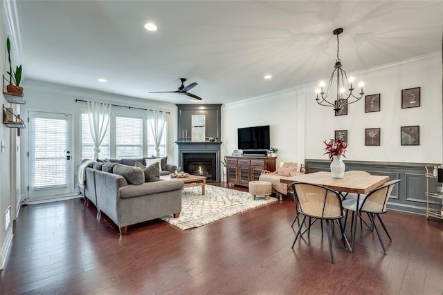 living room featuring a glass covered fireplace, dark wood-style floors, ceiling fan with notable chandelier, crown molding, and recessed lighting