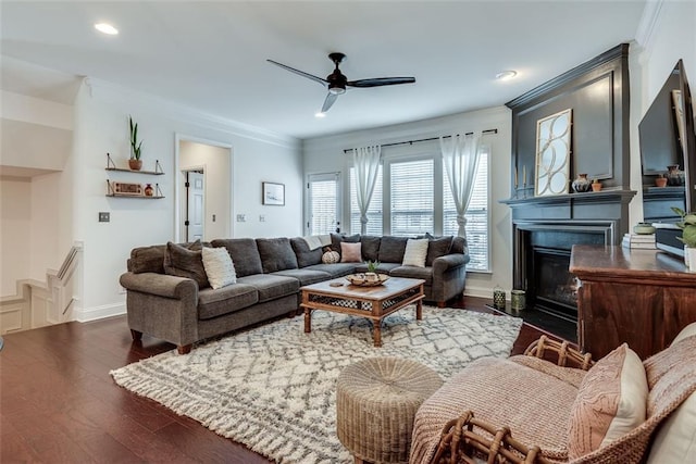 living area with a fireplace with flush hearth, a ceiling fan, baseboards, dark wood finished floors, and crown molding