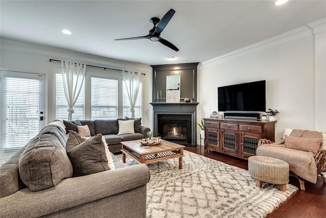 living room featuring dark wood-style floors, ornamental molding, and a glass covered fireplace