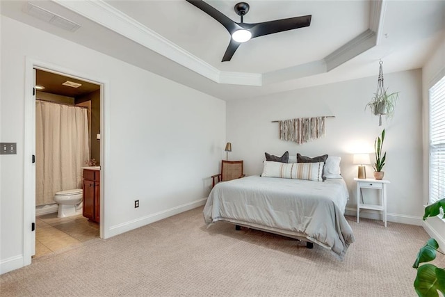 carpeted bedroom with visible vents, baseboards, a tray ceiling, ensuite bath, and crown molding