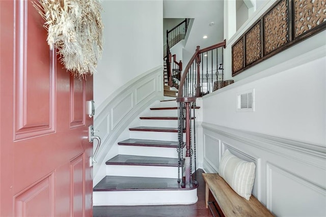 stairs featuring visible vents, a decorative wall, wood finished floors, and wainscoting