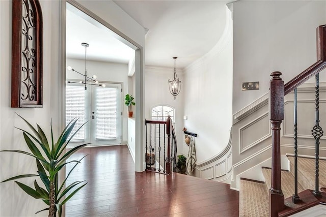 foyer featuring crown molding, a decorative wall, wood finished floors, and an inviting chandelier