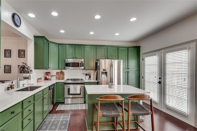 kitchen featuring stainless steel appliances, dark wood-style flooring, a sink, a kitchen breakfast bar, and green cabinetry