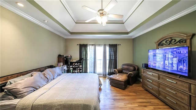 bedroom with ceiling fan, a tray ceiling, light wood-type flooring, and crown molding