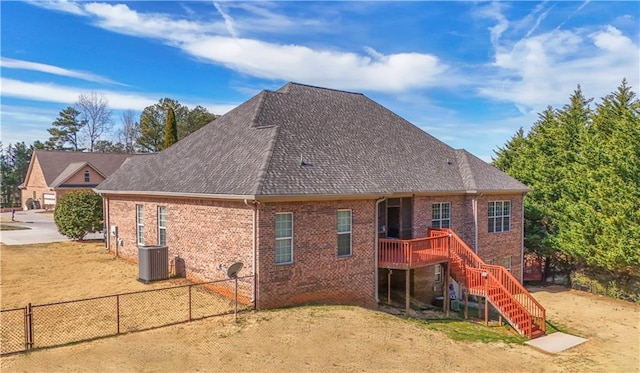 rear view of property with brick siding, a shingled roof, central AC unit, a fenced backyard, and stairs