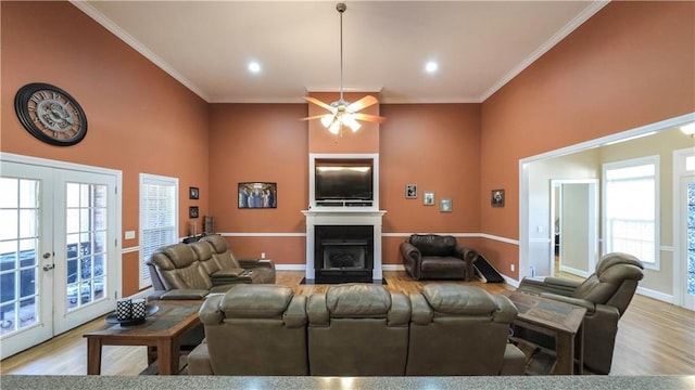 living area with a high ceiling, a fireplace with flush hearth, wood finished floors, french doors, and crown molding