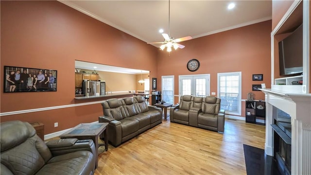 living area featuring crown molding, a fireplace, light wood-style flooring, and a high ceiling