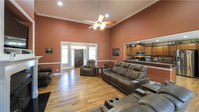 living room with light wood-style flooring, a high ceiling, a ceiling fan, baseboards, and crown molding