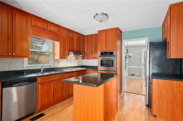 kitchen featuring appliances with stainless steel finishes, tasteful backsplash, sink, a center island, and light wood-type flooring