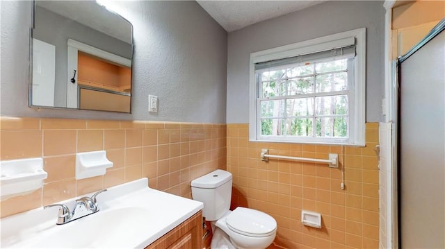 bathroom featuring a textured ceiling, vanity, toilet, and tile walls