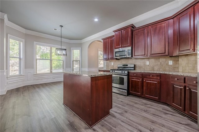 kitchen featuring hanging light fixtures, a kitchen island, light stone countertops, and appliances with stainless steel finishes