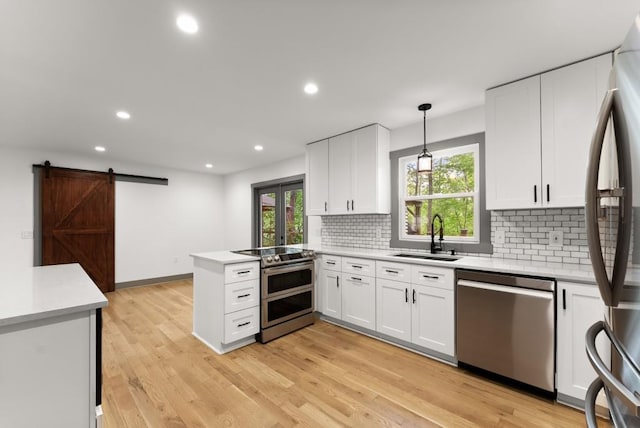 kitchen featuring backsplash, appliances with stainless steel finishes, a sink, white cabinets, and a peninsula