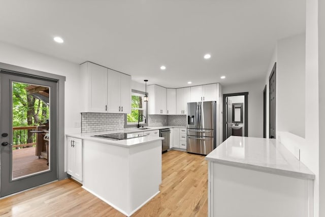 kitchen featuring a sink, light wood-style floors, a peninsula, decorative backsplash, and black appliances