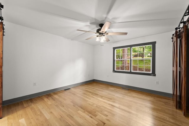 empty room featuring baseboards, a barn door, light wood finished floors, and ceiling fan