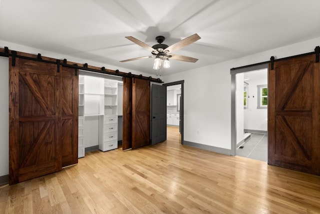 unfurnished bedroom with baseboards, ensuite bath, light wood-type flooring, and a barn door