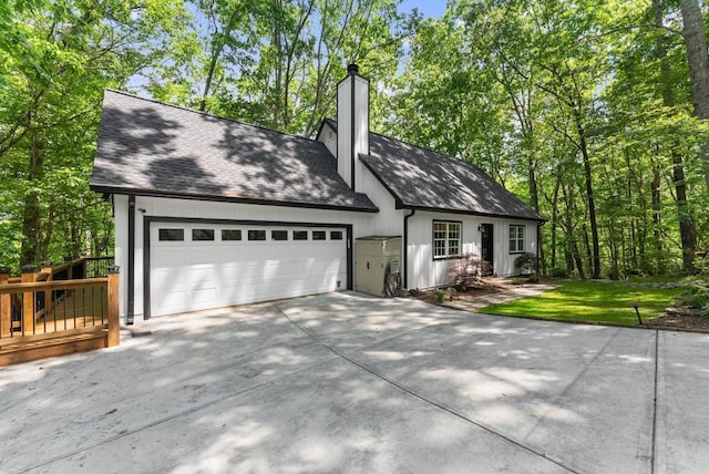 view of front of home with an attached garage, driveway, a chimney, and roof with shingles