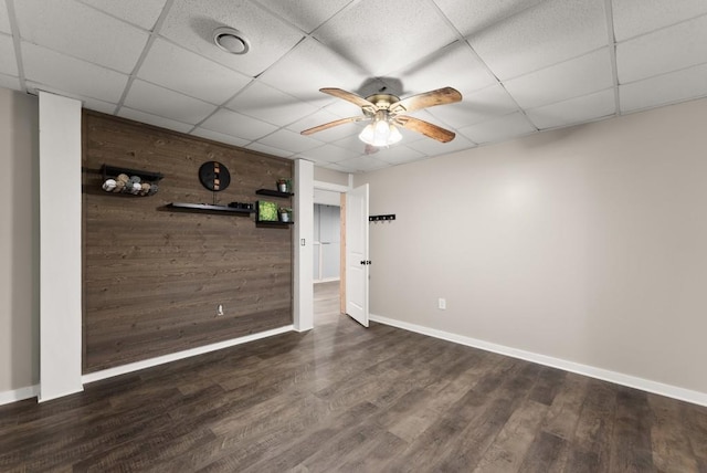 spare room featuring wooden walls, baseboards, a ceiling fan, and a drop ceiling