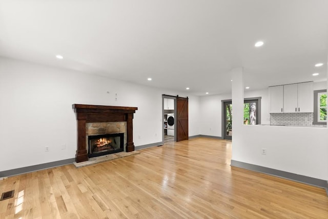 unfurnished living room with washer / clothes dryer, light wood-type flooring, a barn door, baseboards, and recessed lighting