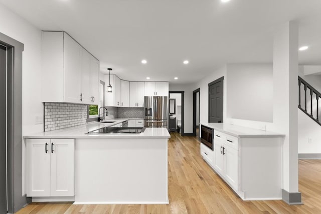 kitchen featuring a peninsula, stainless steel refrigerator with ice dispenser, light countertops, built in microwave, and a sink