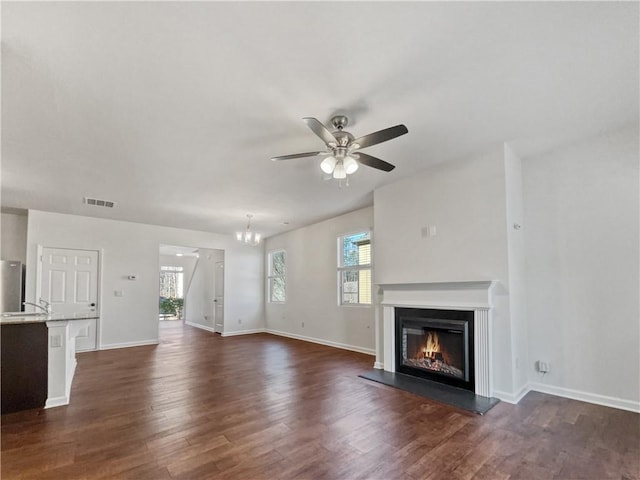 unfurnished living room with ceiling fan with notable chandelier, plenty of natural light, and dark wood-type flooring