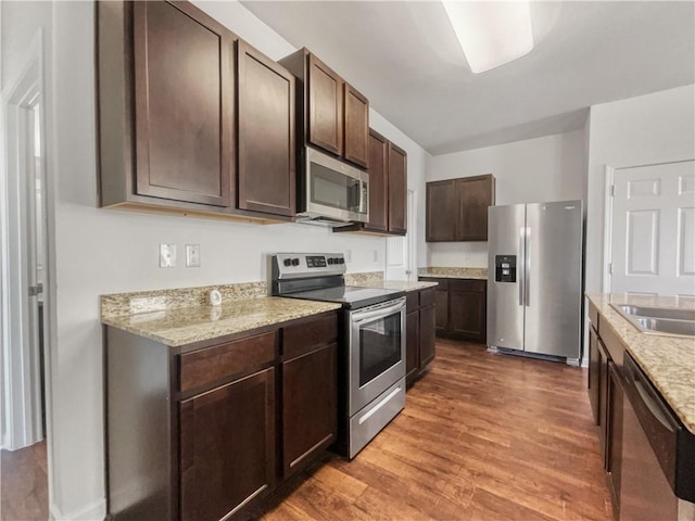 kitchen with stainless steel appliances, sink, light stone counters, hardwood / wood-style flooring, and dark brown cabinets