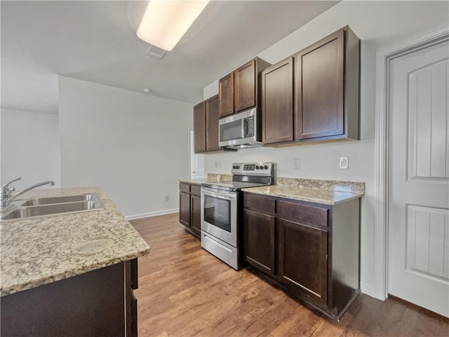 kitchen featuring light stone countertops, stainless steel appliances, light wood-type flooring, dark brown cabinets, and sink