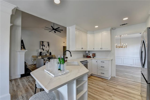 kitchen with kitchen peninsula, pendant lighting, stainless steel appliances, ceiling fan with notable chandelier, and white cabinets