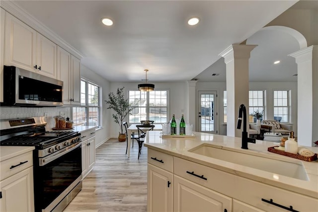 kitchen with appliances with stainless steel finishes, decorative columns, white cabinetry, sink, and hanging light fixtures