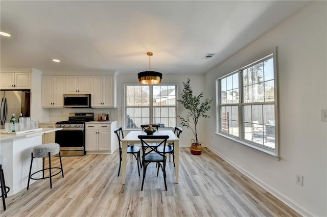 kitchen with stainless steel appliances, white cabinetry, light wood-type flooring, and decorative light fixtures